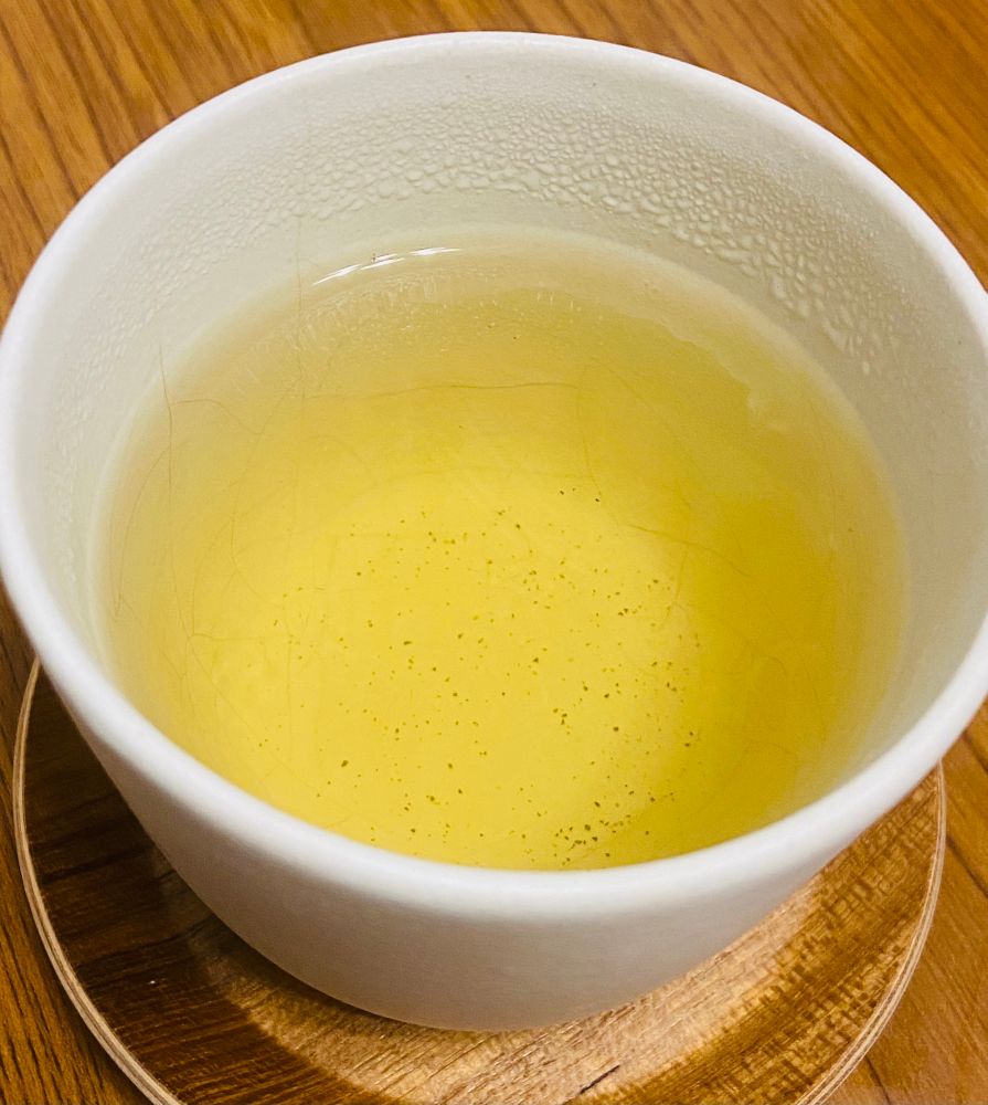 白い茶器の中に薄黄色の梨山茶が入っている。それを木製の茶托で受けている。