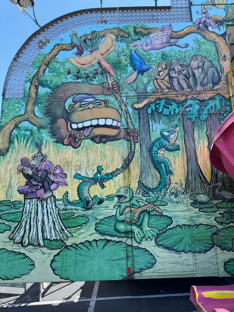 A trippy mural on the side of a carnival funhouse of a bog and assorted animals, all looking stoned.