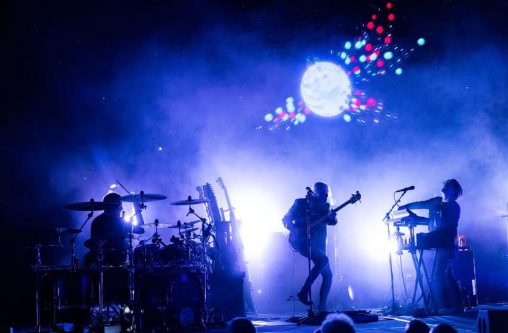 Steven Wilson concert in 2025 - three of the band (Craig Blundell, drums; Nick Beggs, bass; Steven Wilson, vocals/guitars/keyboards) caught mid-song and mid-movement in a blue and purple light.  
Photo by Diana Seifert, Paris.