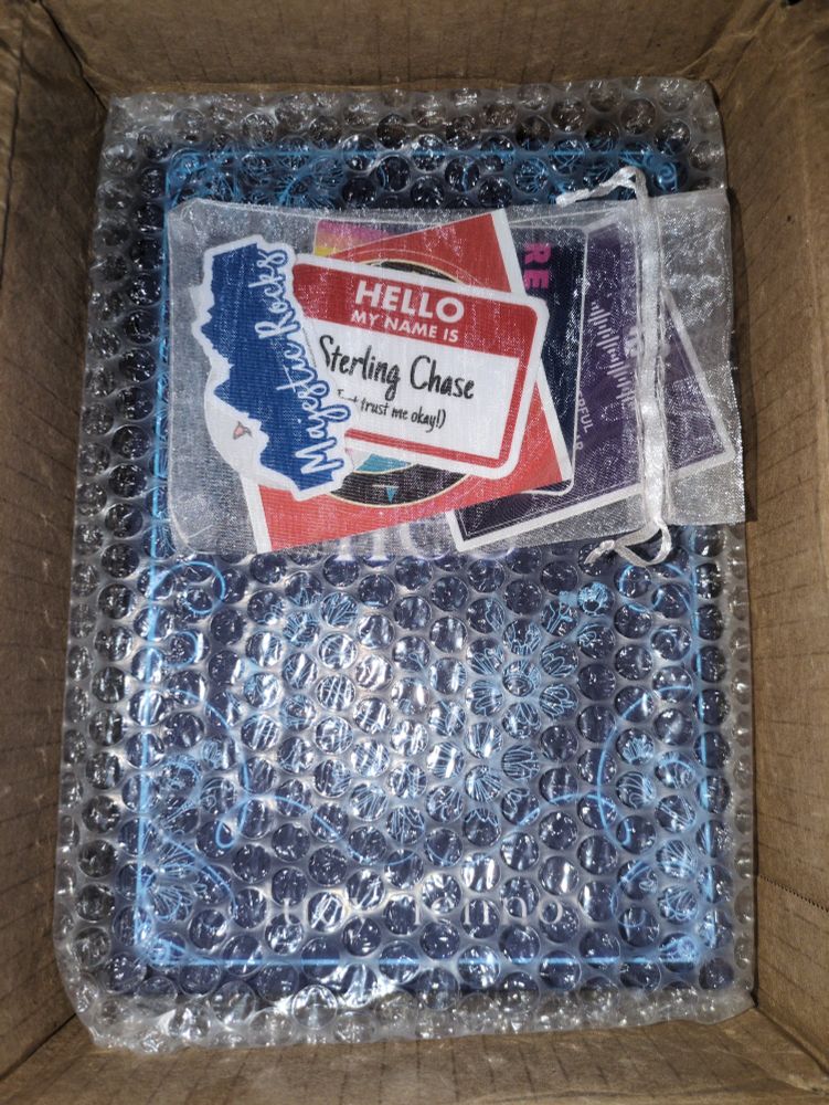 Sticker pack on top of bubble wrapped covered books in an opened box.