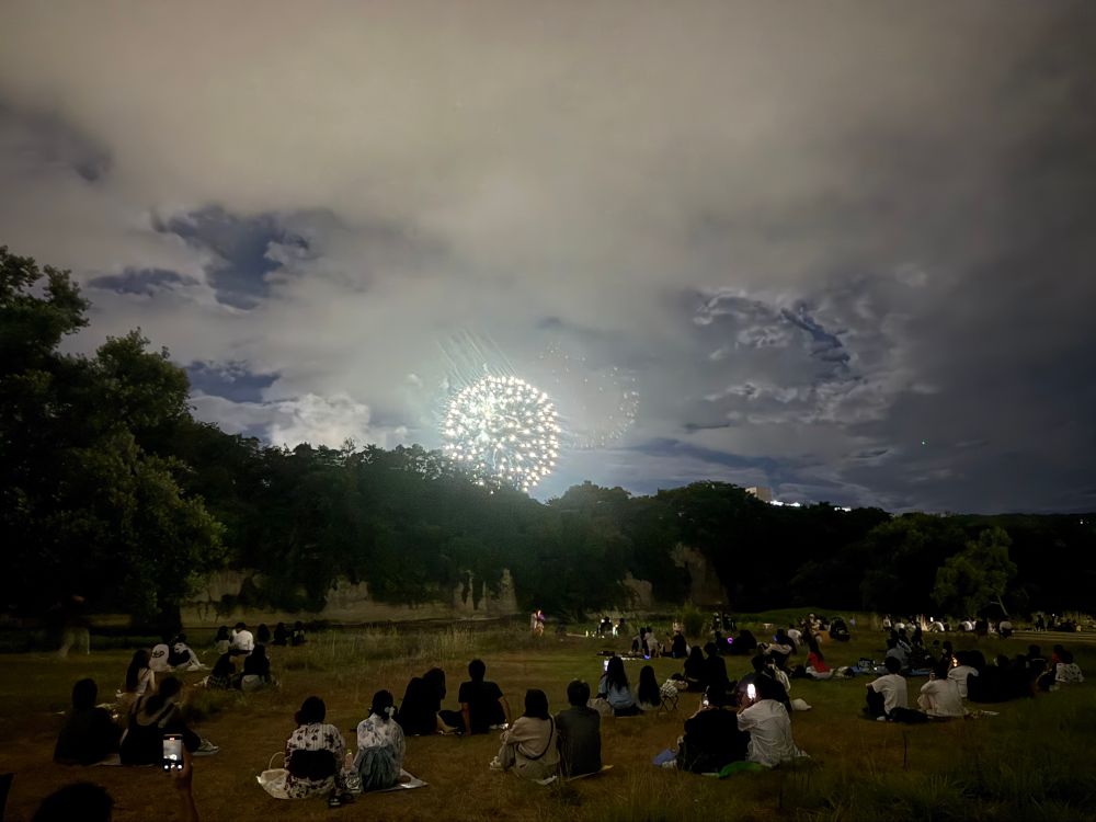川べりに人びとが座って花火を眺めている。