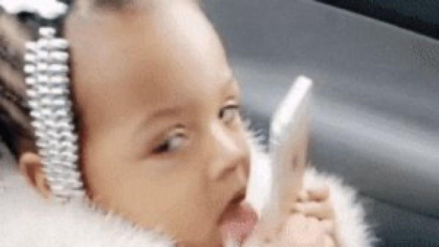 Meme of a little girl licking an iPhone while making eye contact with the person taking the photo 