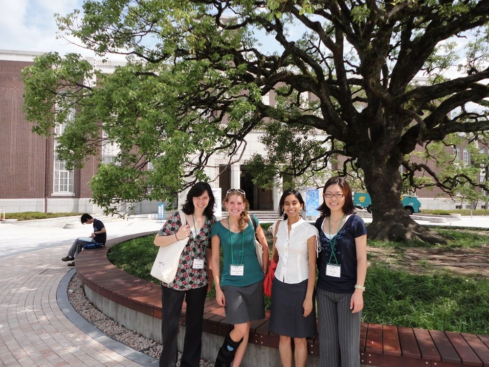 Four scientists wearing conference badges standing in front of a big tree at a conference venue. 