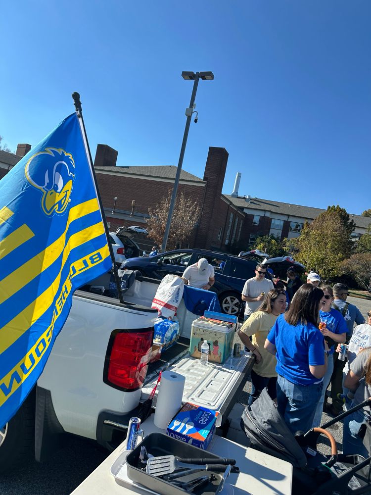 Photo of a tailgate behind a pick up truck with people standing around on a blue sky day in Newark, Delaware