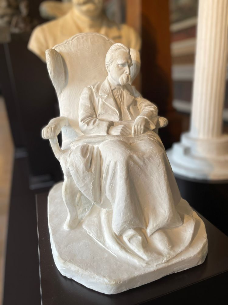 White plaster statuette of the infirm Friedrich Nietzsche in an armchair with a blanket over his legs