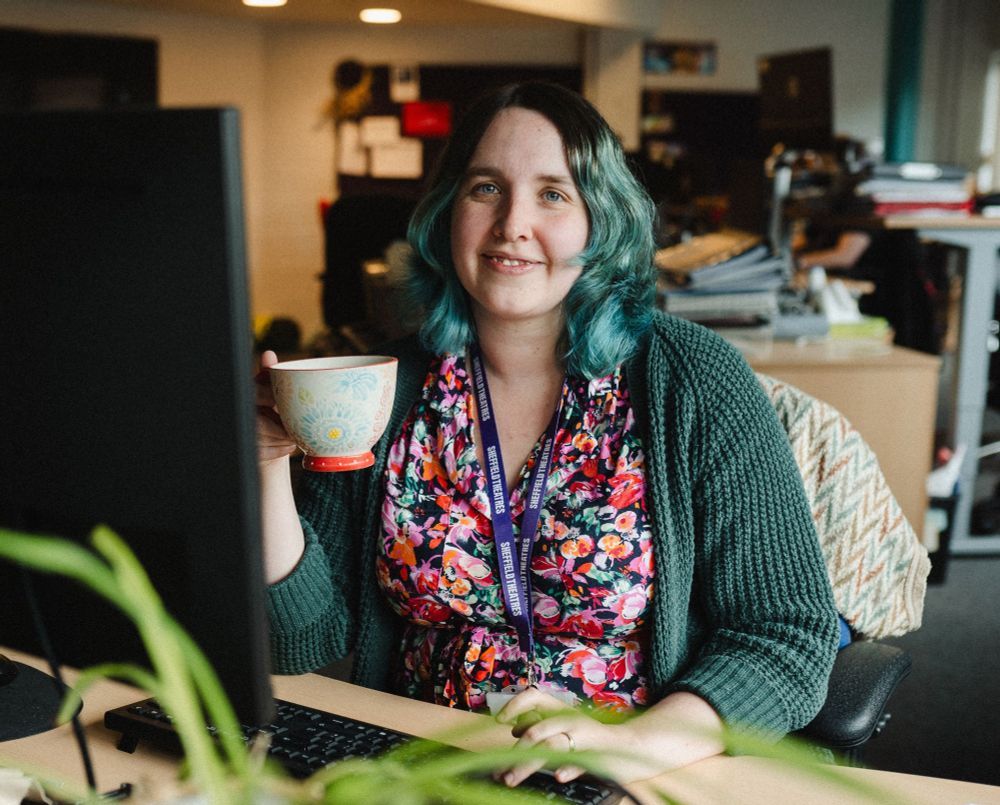 A photo of me at work, smiling at the camera and holding a cup of tea 