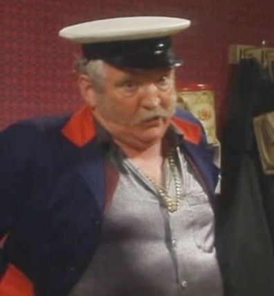 Milkman Pat Mustard from Father Ted: an ageing white man in a milkman's hat and blue jacket; he has a grey moustache and unruly sideburns. He is wearing a gold chain round his neck and his jacket is open to reveal a silky silver shirt.