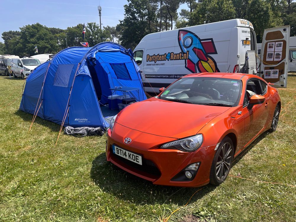Orange gt86 parked in front of a blue tent on a campsite 