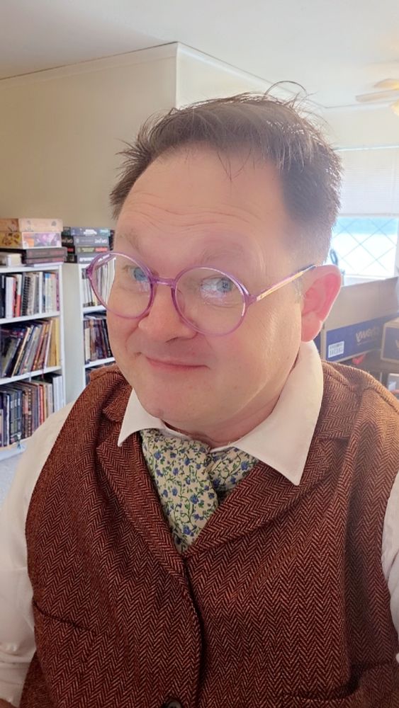 Me smiling, wearing a white shirt, orange vest, and blue floral neckerchief. 