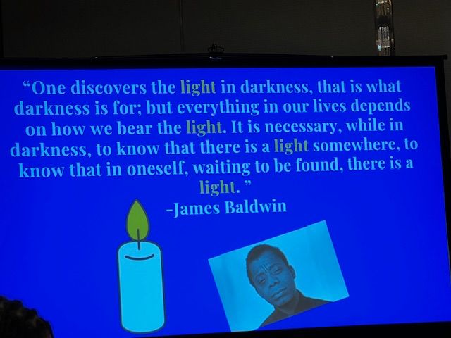 Photograph of a slide: "One discovers the light in darkness, that is what darkness is for; but everything in our lives depends on how we bear the light. It is necessary, while in darkness, to know that there is a light somewhere, to know that in oneself, waiting to be found, there is a light. -James Baldwin" photo of candle & picture of James Baldwin