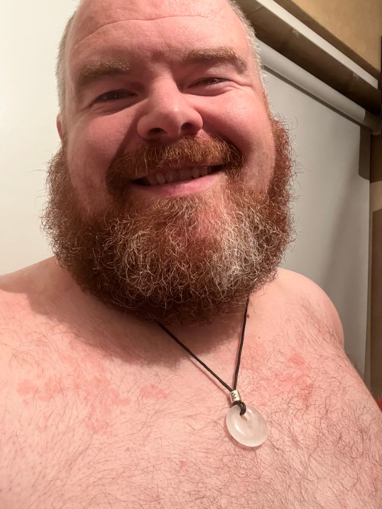 Man with beard, shirtless with necklace and smiling. 