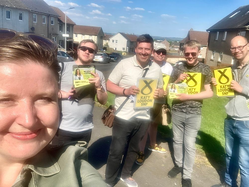 A selfie of people standing on a street with yellow SNP signs