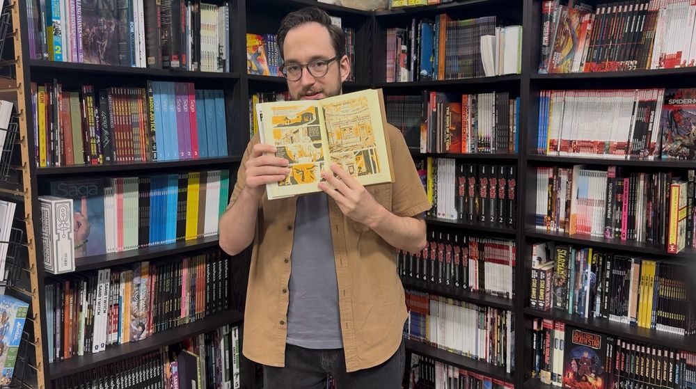 Chris Condon stands in the Stacks at Third Eye Comics in Annapolis, Maryland. He's holding open a copy of Darwyn Cooke's PARKER: THE SCORE.