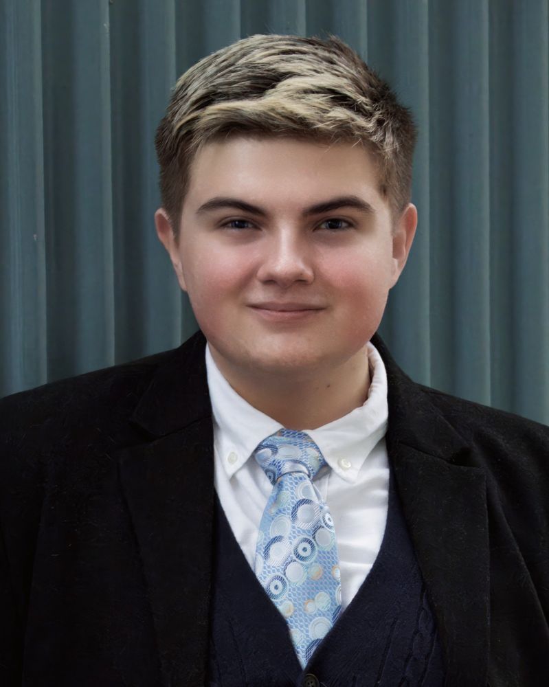Head-and-shoulders shot of the same young man in front of a blue/grey corrugated metal wall. 