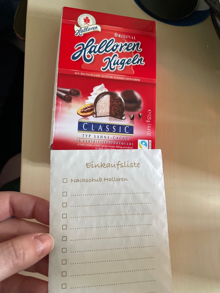 Inlay einer Halloren-Pralinenpackung mit einer aufgedruckten Einkaufsliste. An erster Stelle steht „Nachschub Halloren“.
