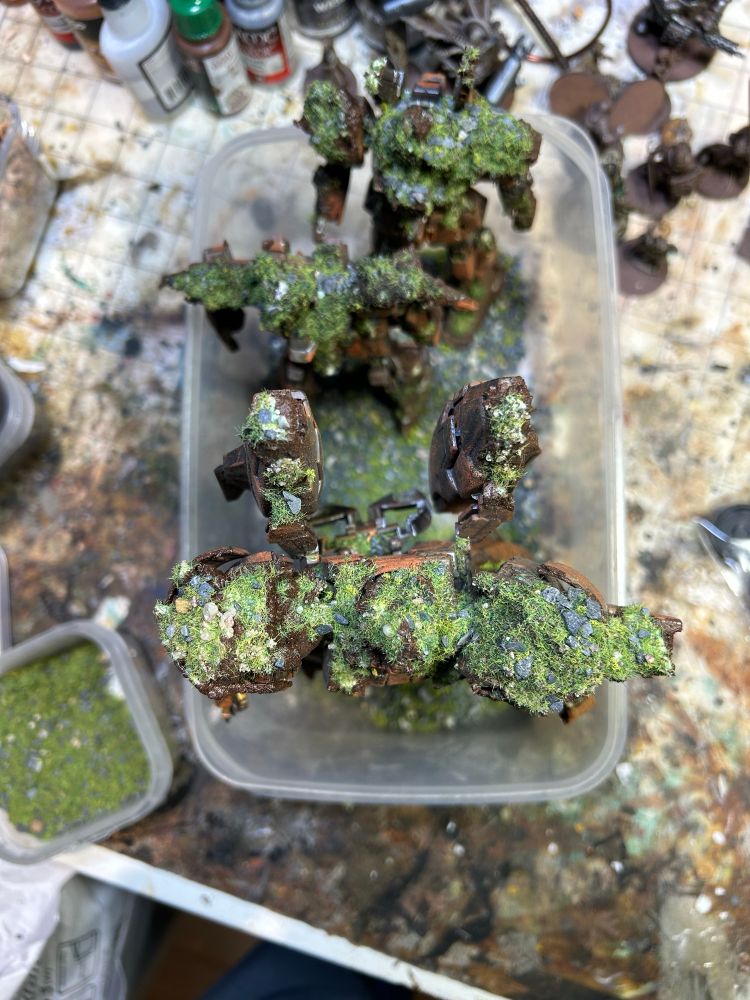 A top down view of three robot kits in a plastic tub having basing material glued to them. 