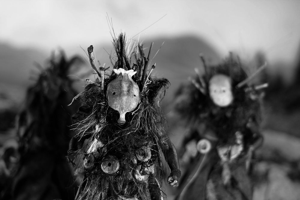 A black and white image from Pine Pitch Black, the monochrome version of Maskwitches. A moody shot of a witch with a seed pod mask. In the background are two other witches out of focus. 
