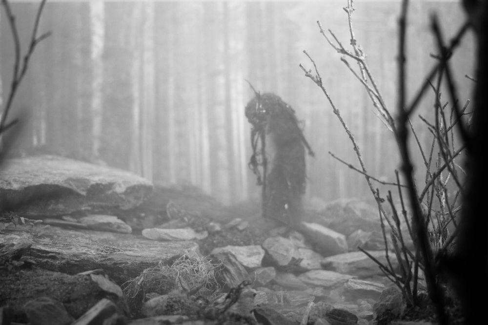 A black and white image from Pine Pitch Black, the monochrome version of Maskwitches. An evil spirit lurking in the woods
