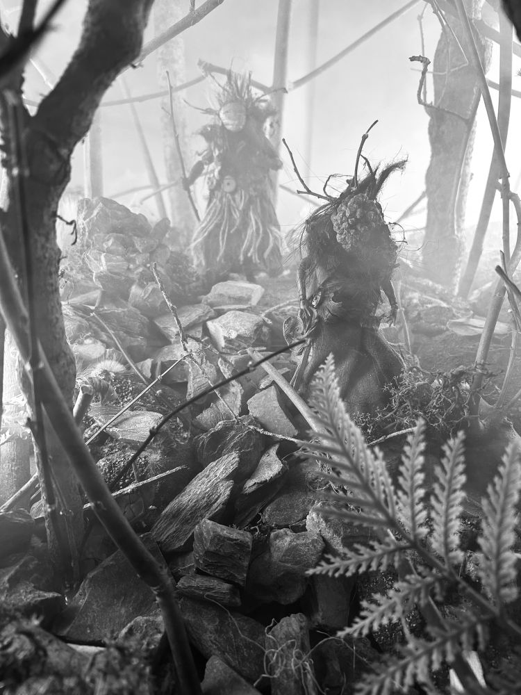 A black and white image from Pine Pitch Black, the monochrome version of Maskwitches. Some witches move through the forest. 