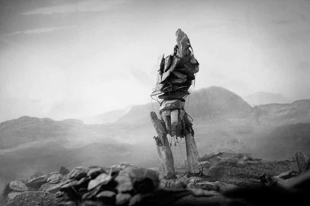 A black and white image from Pine Pitch Black, the monochrome version of Maskwitches. An evil spirit made of stones. It appears to have no arms. 