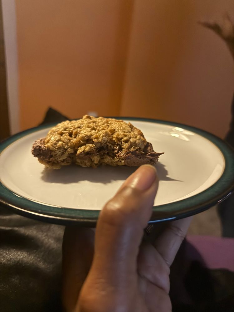 On a white plate with green trim sits a homemade oatmeal cream pie that I have bitten into to share with you all its deliciousness. 