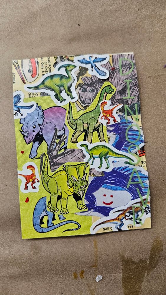 This collage is made up of a number of dinosaur stickers layered over one another. The dinosaurs include the Tricératops, raptors, brontosaurus, and arcteryx. There is also a scribbled blue face with blue hair, outline, and red eyes and mouth. Stickers on the right side write the word 'DINOSAUR' vertically. 