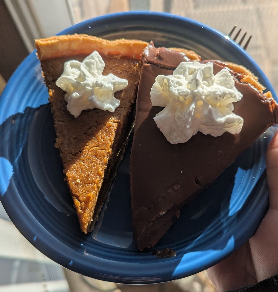 A slice of homemade sweet potato pie and a slice of homemade chocolate fridge pie, each adorned with a little star of whipped cream, on a blue fiestaware plate.