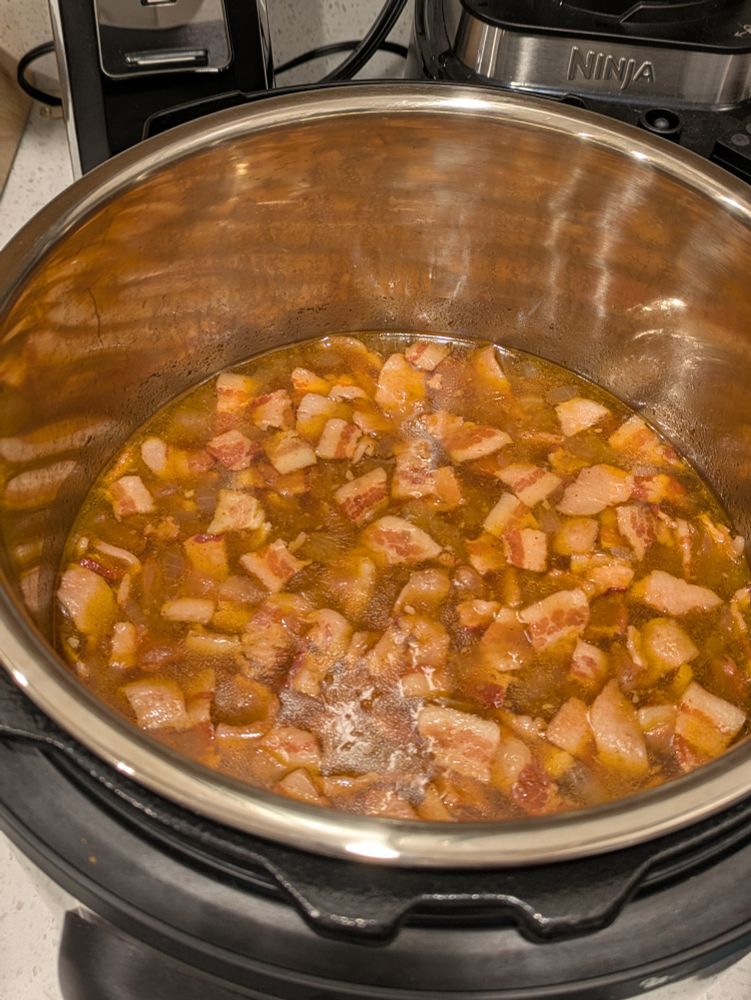 An instant pot containing a pot of cooked beans, onions, and small bacon pieces.