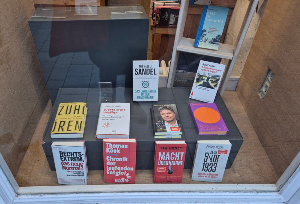 Bücher im Schaufenster eines Buchladens. Titel "5 vor 1933", "Machtübernahme", "Chronik der laufenden Entgleisung", "Rechtsextrem, das neue Normal?", "Zuhören - die Kunst, sich der Welt zu öffnen", "Worte statt Waffen", "Den Bach rauf", "Werte. Ein Kompass für die Zukunft", "Das Unbehagen in der Demokratie", "Schuldenbremse oder 'goldene Regel'?" und "Exil im Paradies"