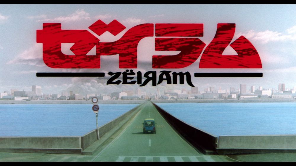 Zeiram title card featuring the title in bold red Japanese characters with the title in English (stylized: ZËIЯAM) over a shot of a road extending over a body of water to a cityscape in the distance with a sinister cloud in the form of the key antagonist, Zeiram. On the causeway: a vehicle drives away from camera, toward the city.
