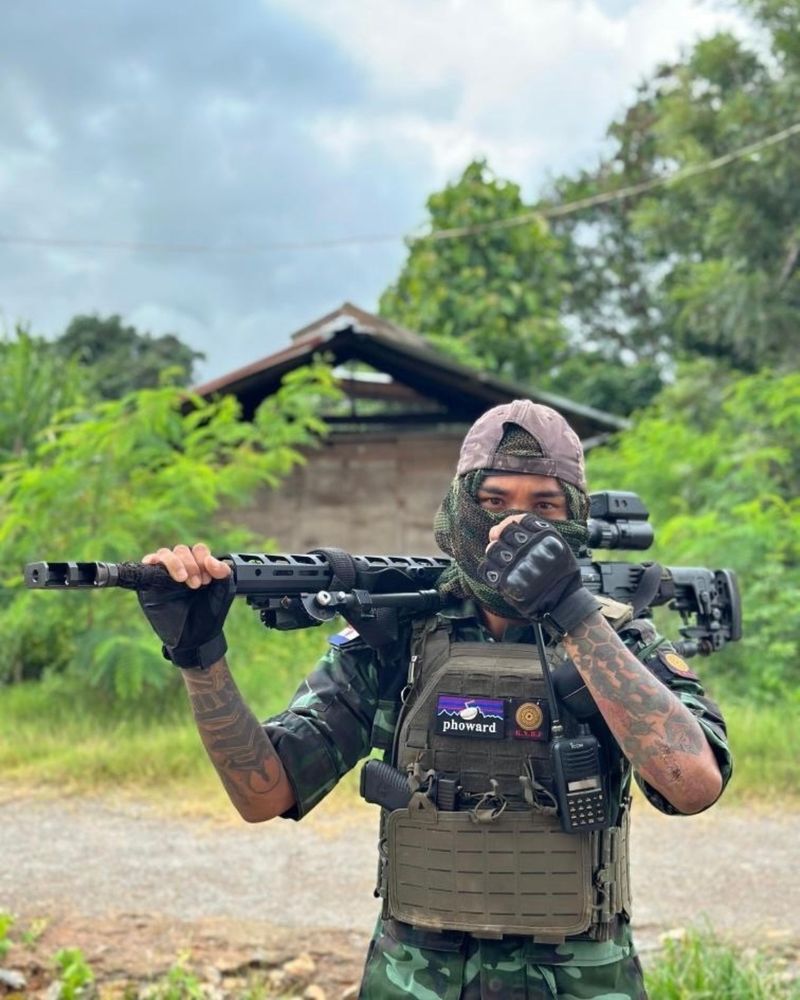 A Karenni fighter geared up. He has a pistol and radio and plate carrier. He is covering his face holding a long-range rifle