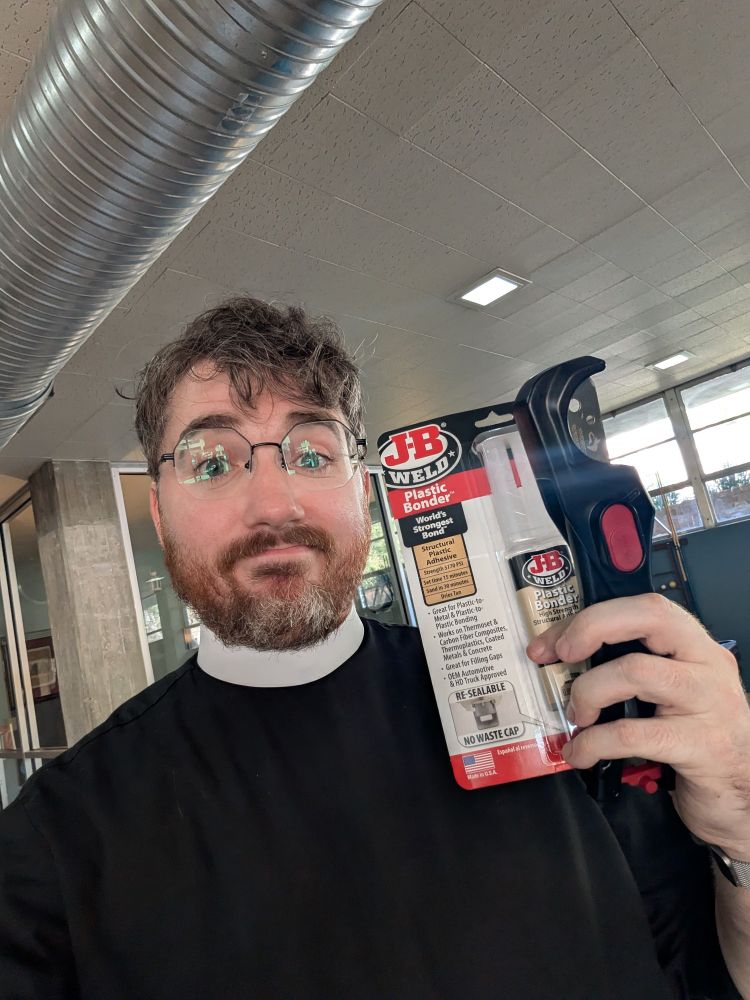 A man in a clergy collar holding a tube of epoxy and a tool for cutting plastic piping