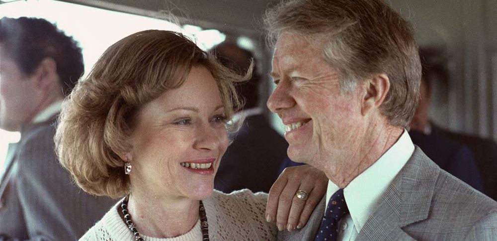 Rosalynn Carter with her hand on Jimmy Carter’s shoulder, gazes lovingly at her smiling husband. Photo via the Carter Center.