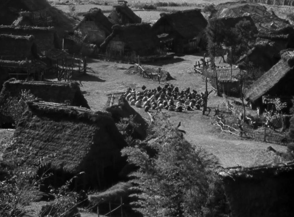 An early image from Akira Kurosawa's Seven Samurai looking down at the farming village with the villagers crowded in a circle in the middle of town. 