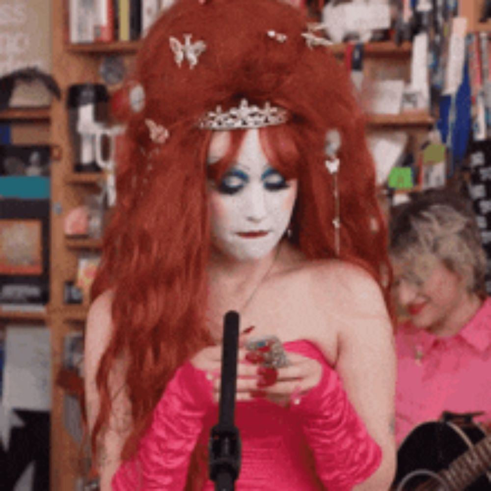 a woman with red hair and a crown on her head is holding a microphone