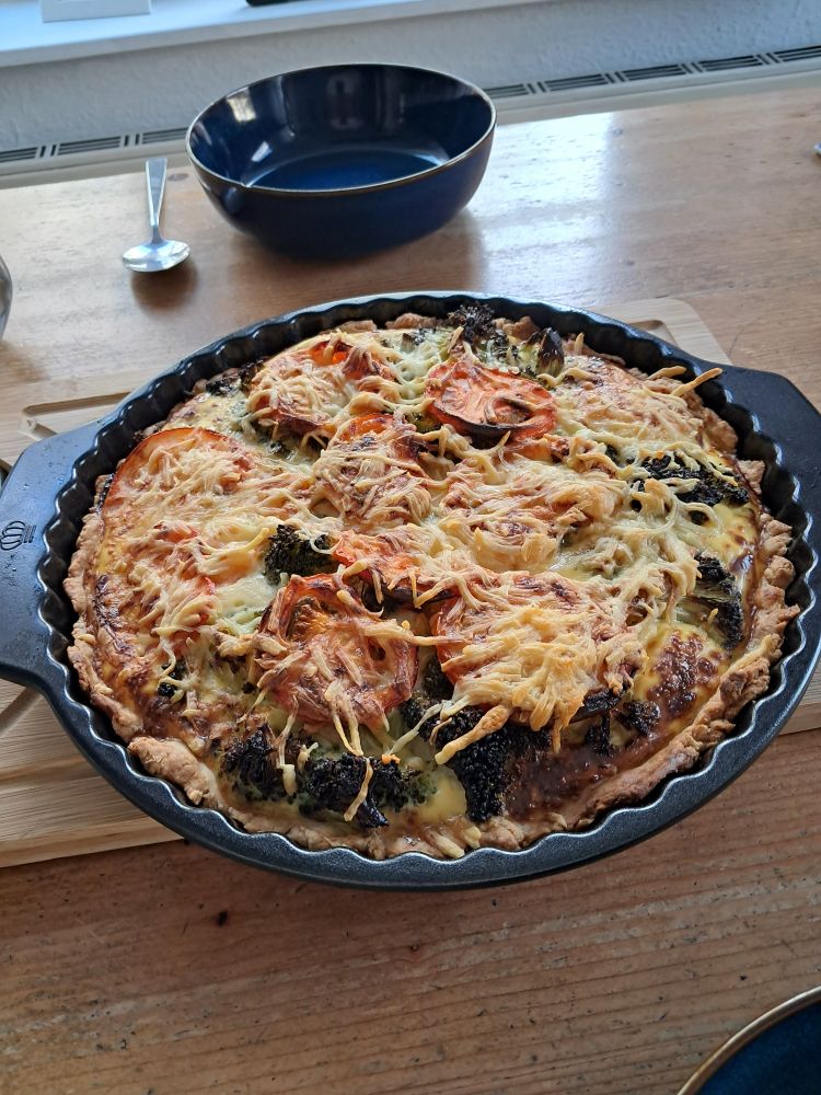 Eine Quicheform mit Teigboden und -rand, gefüllt mit Brokkoli, Tomaten, Eier-Sahne-Masse und mit Emmentaler überbacken.