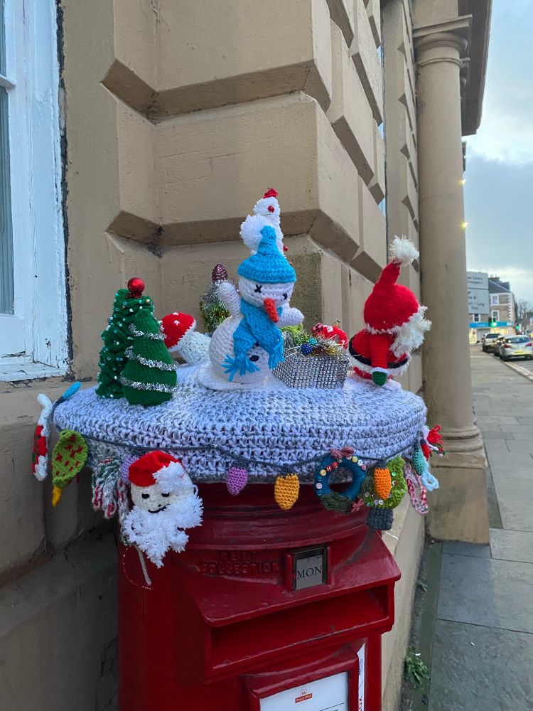 Crocheted Christmas figures - Santa, Snowman - and other festive objects decorating a postbox 
