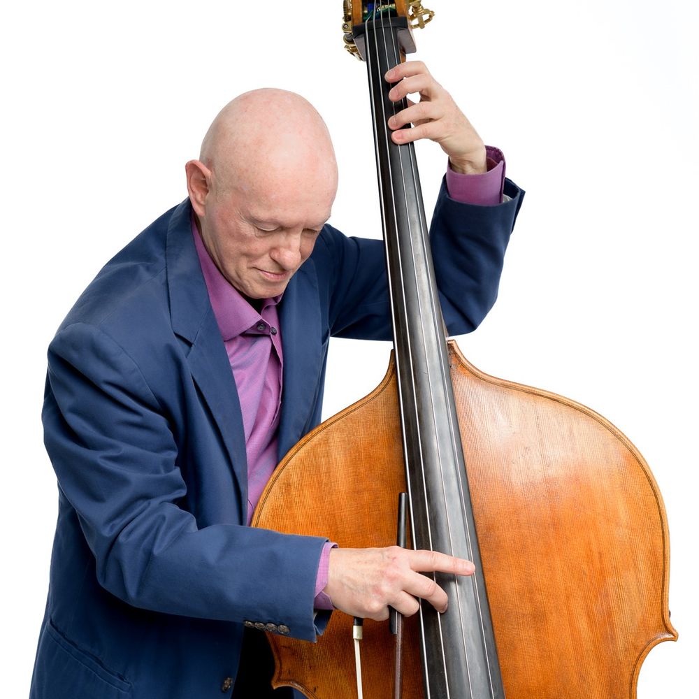 This is a portrait of Mark Bernat playing his double bass. Mark is a caucasian man wearing a blue jacket over a purple shirt. Background is white