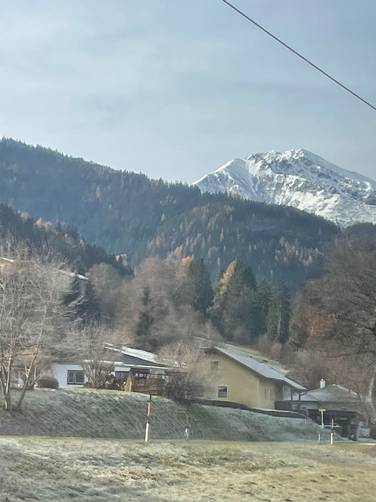 Blick aus dem Zug, ländliche Gegend, Hügel, Häuser, Wald dahinter verschneiter Gipfel 
