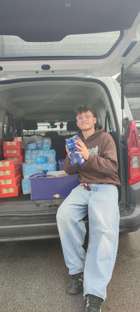 Unser Volunteer Franz beim Ausladen des VANs, um die eingekauften Lebensmittel in unser Warehouse zu schichten. Für Samstag werden sie dann in die jeweiligen Pakete gepackt.
Franz trägt Jeans, braunen Pullover, kurze Haare, Brille. Im Auto: Mehl, Tomatensauce, Pasta. 
