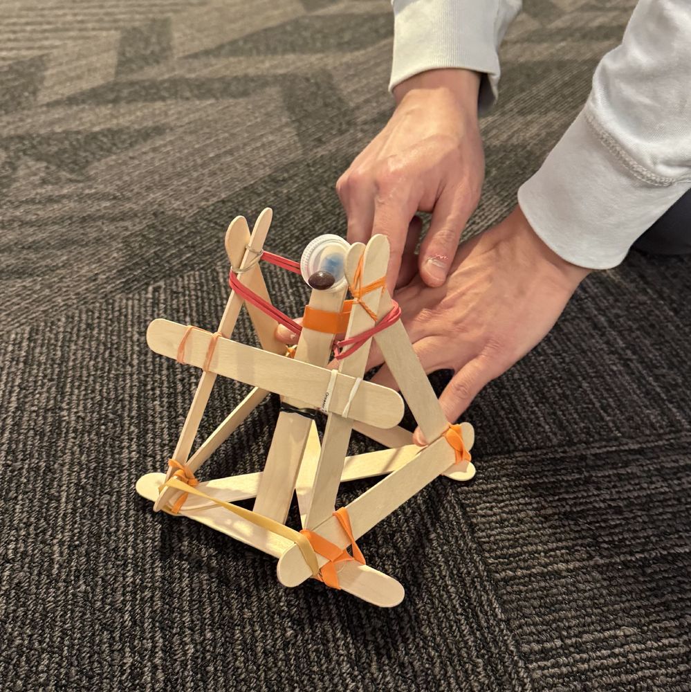 A Skittle catapult built with popsicle sticks, rubber bands, and a water bottle cap.