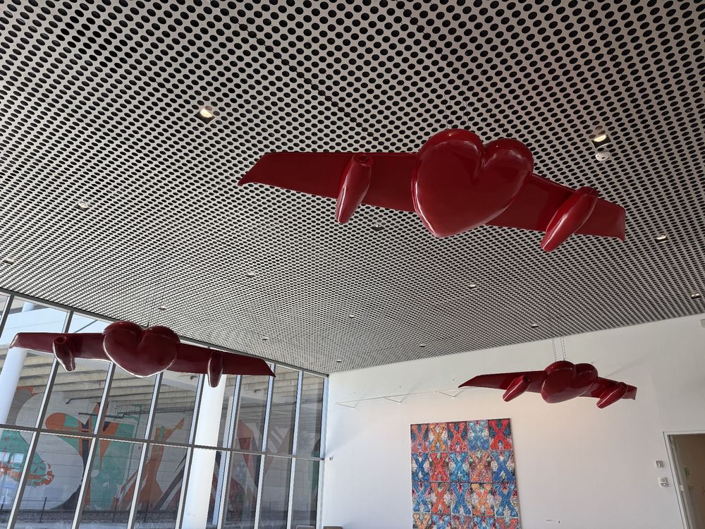 Photo of Estero Segura’s “Goodby My Love” in the Tampa Museum. Three red hearts with airplane wings, hanging from the museum ceiling.