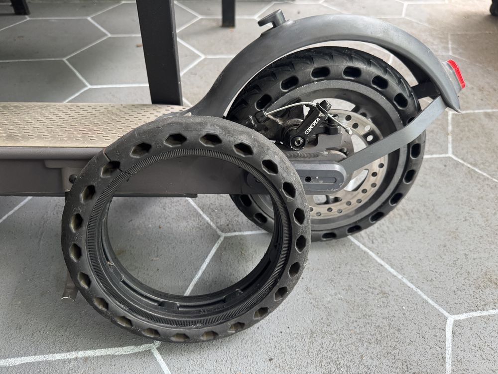 Photo of a removed solid rubber tire next to the rear of an electric scooter with a new tire installed.