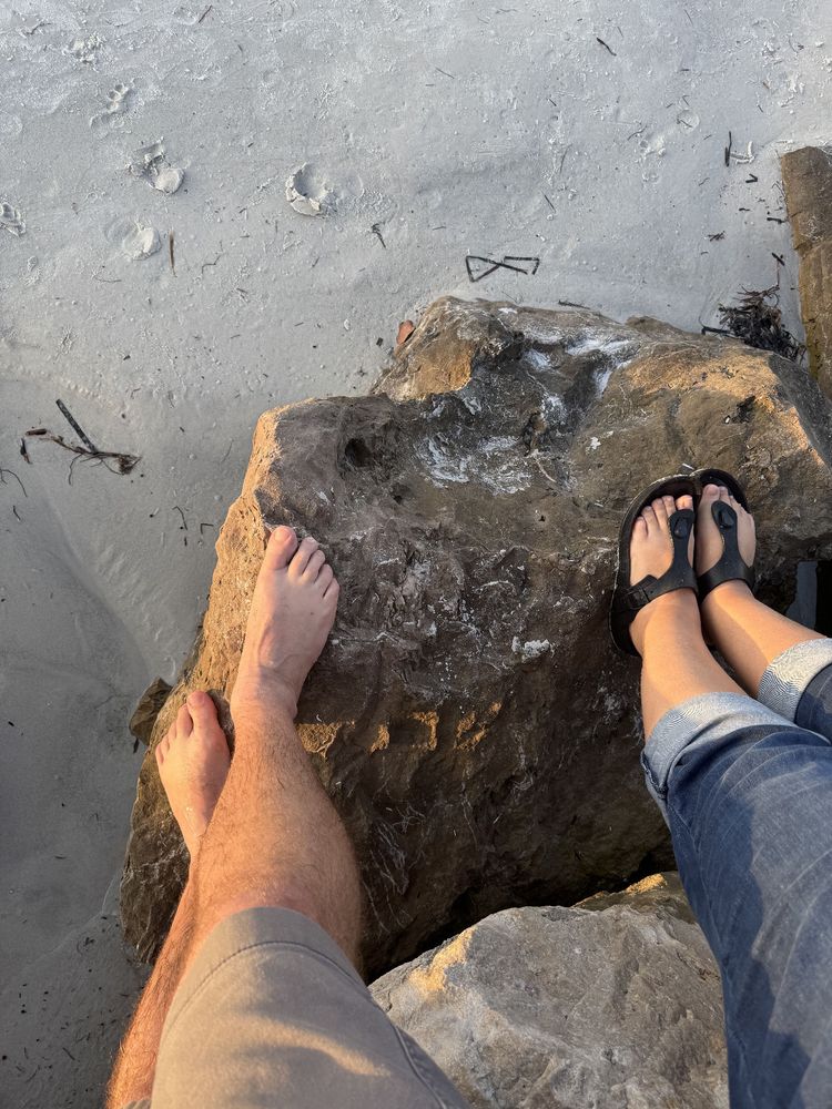 Photo of our feet standing on a rock together at the beach.
