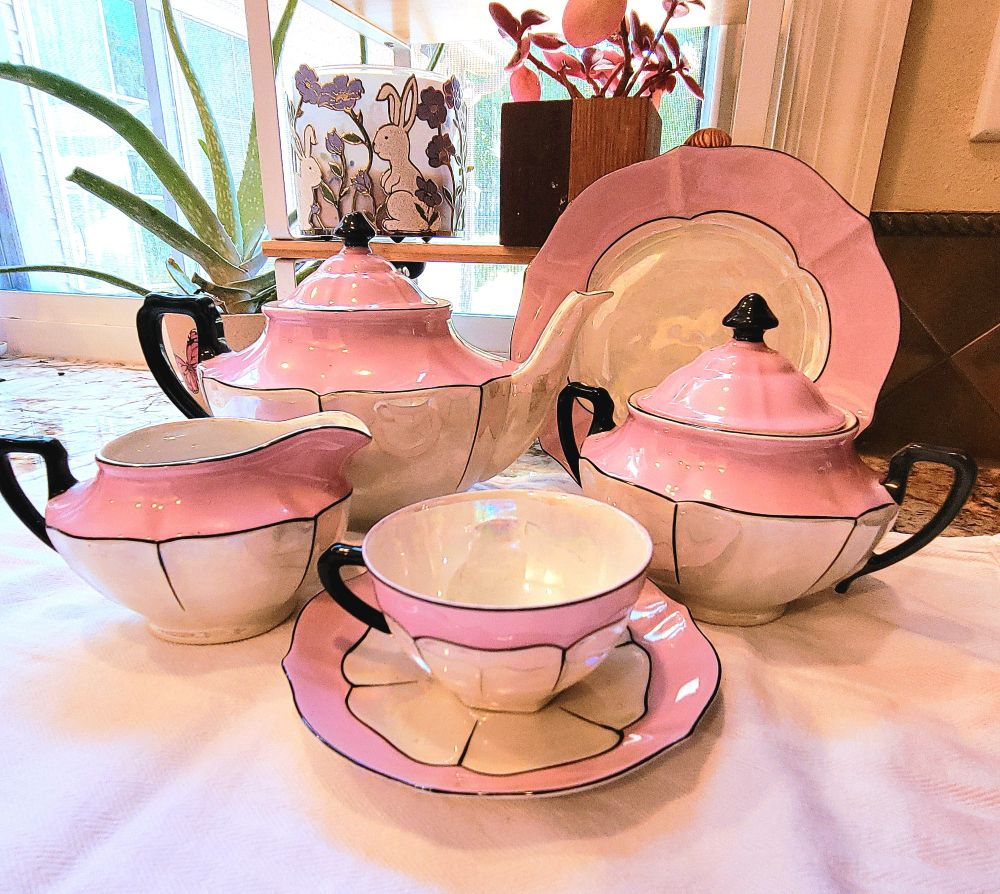 Several pieces of "lusterware", 1920s art deco style tea set. There is a teapot, creamer pitcher, sugar bowl, dessert plate, tea cup & saucer. They are light pink on top, white opalescent on bottom with black handles and details. 
