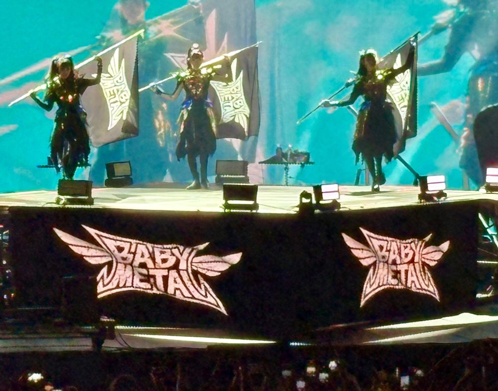 Babymetal on stage holding Babymetal flags with Babymetal logos on screens