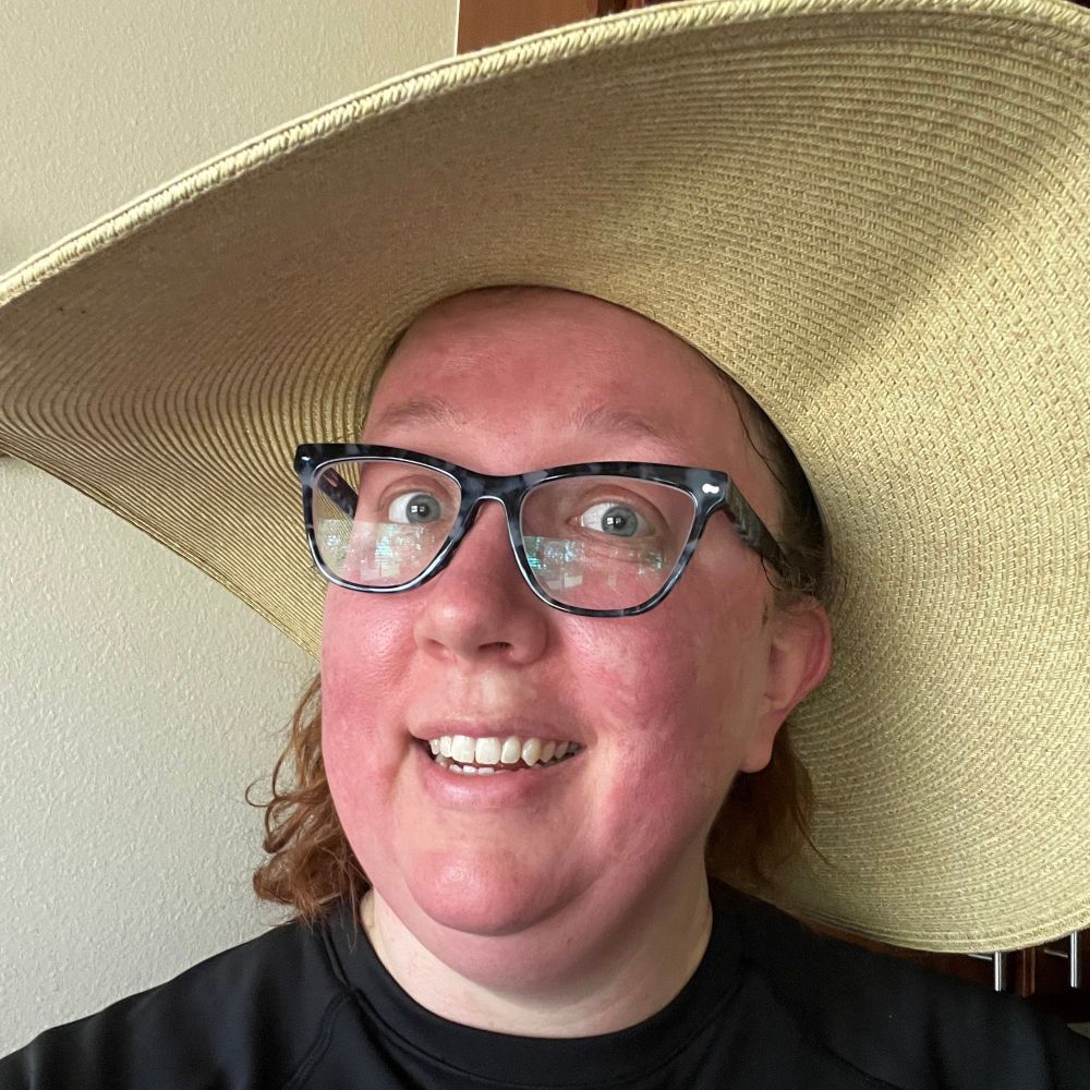 A white woman with a very red face in an oversized hat. 
