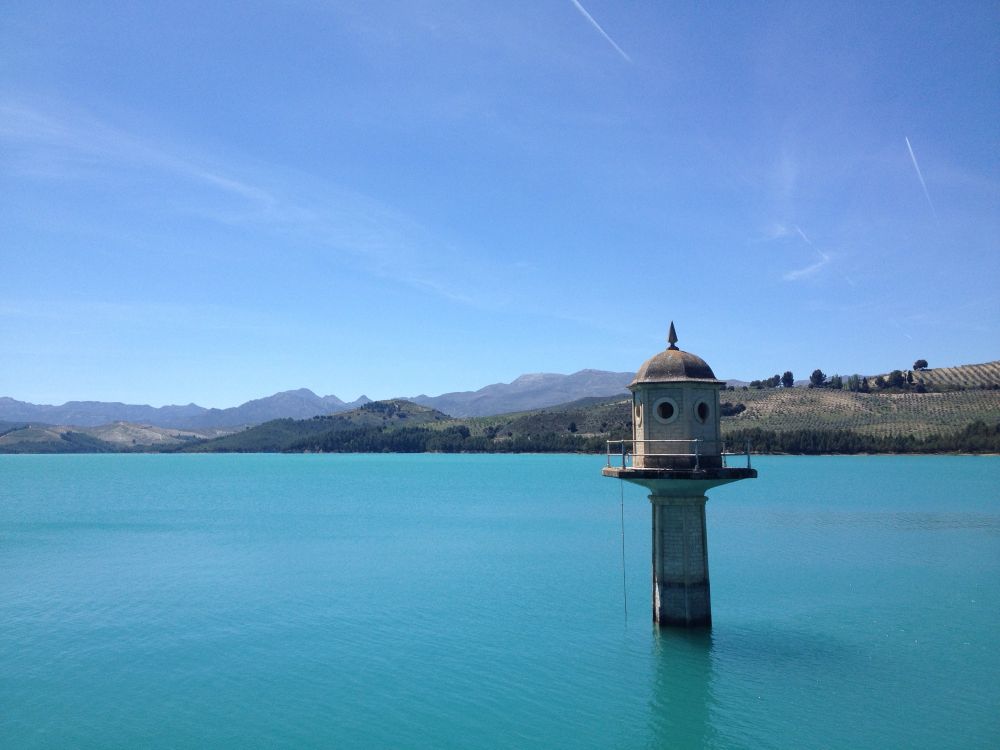 Deep blue coloured water of a reservoir in Andalusia, with the tip of a stone watch tower peeking out above the water. 