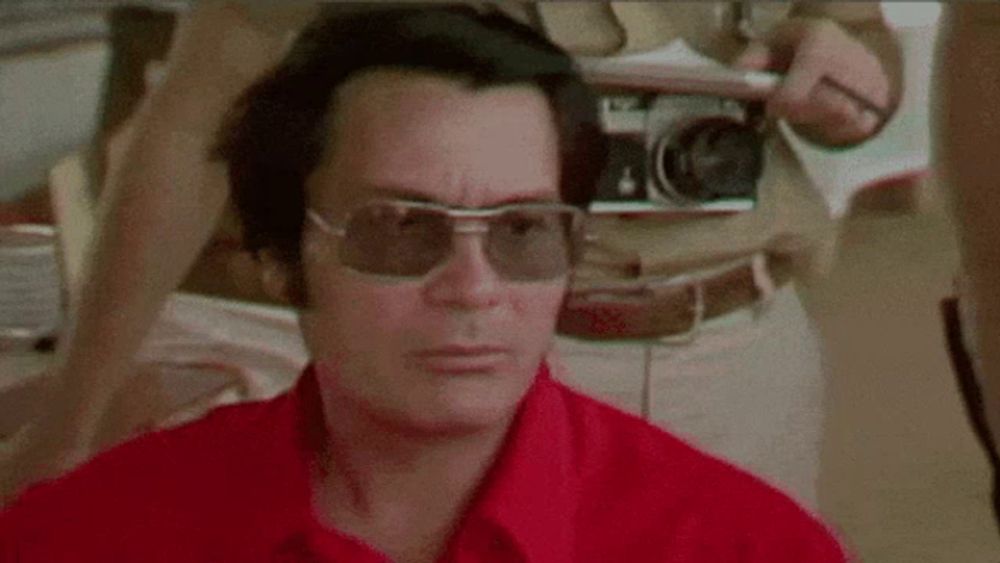 a man wearing sunglasses and a red shirt is standing in front of a camera