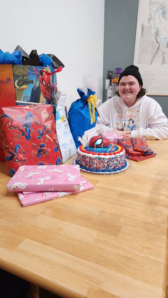 And 18 year old girl sits with her Spiderman birthday cake surrounded by wrapped gifts.